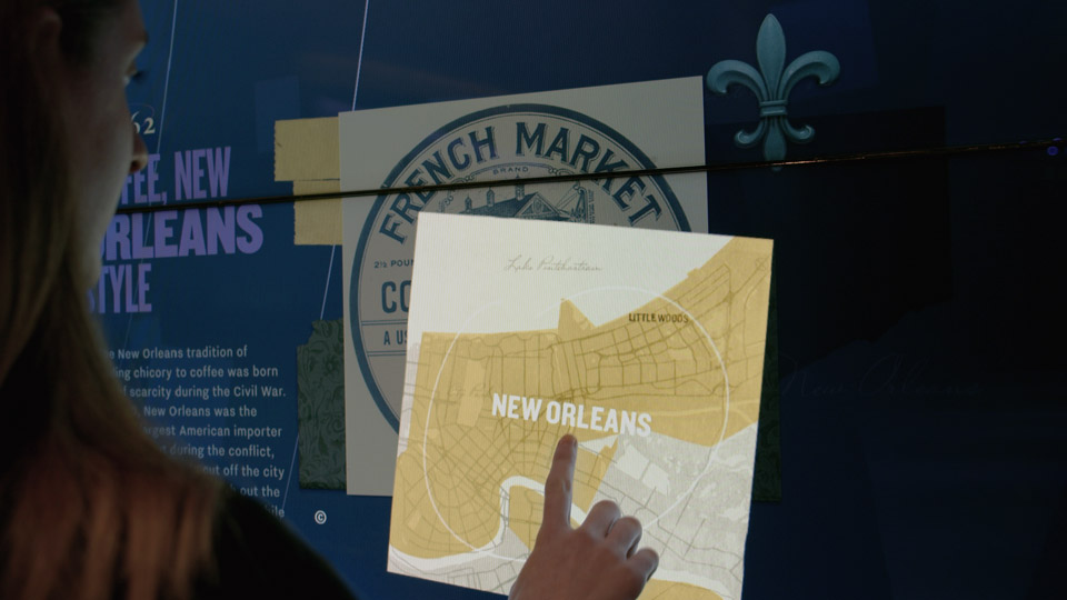 Visitor opening a French Market card on the touch wall, revealing a hand-drawn New Orleans map